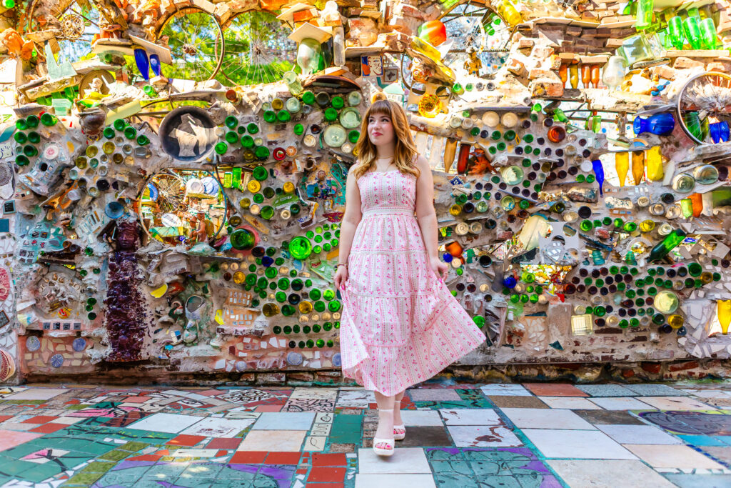 A Philadelphia senior session with a girl with red hair twirling her pink and white dress in front of a vibrant mosaic wall at The Magic Gardens.