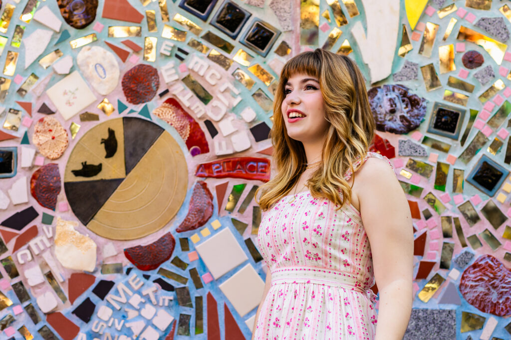 Side profile senior portrait of Lyla looking upward in front of detailed mosaic artwork.
