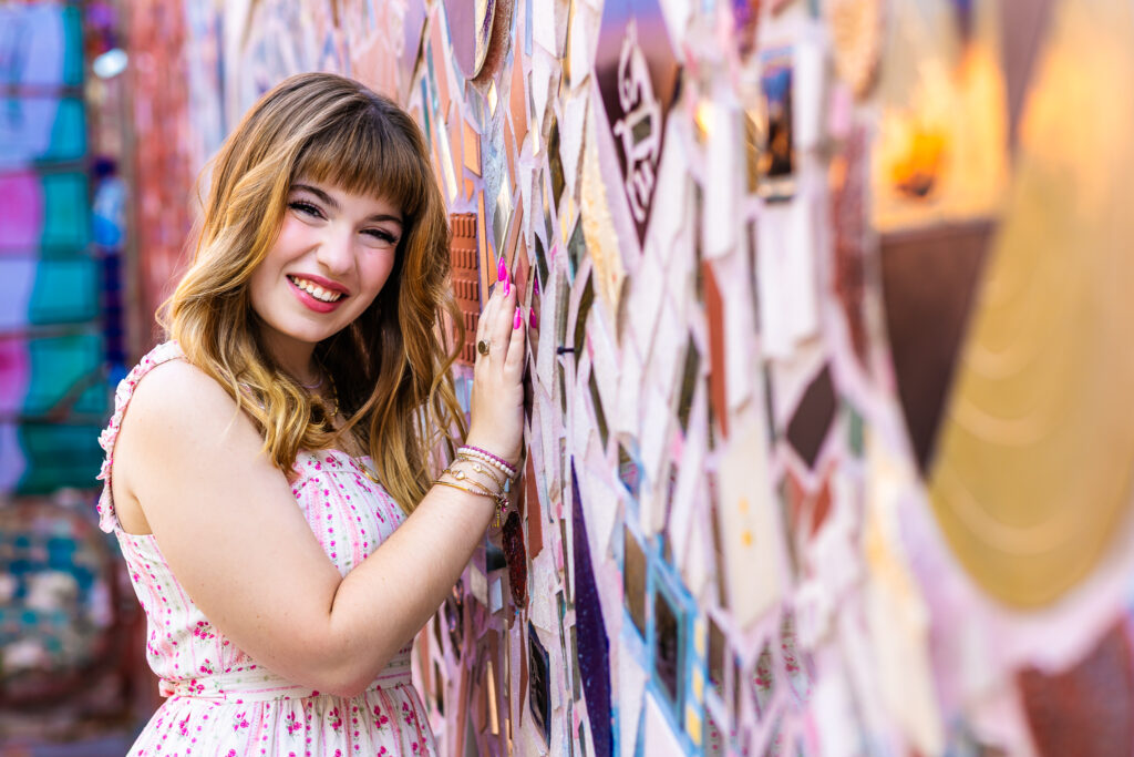 Portrait of Lyla smiling while leaning against a textured mosaic wall during a Philadelphia senior session.