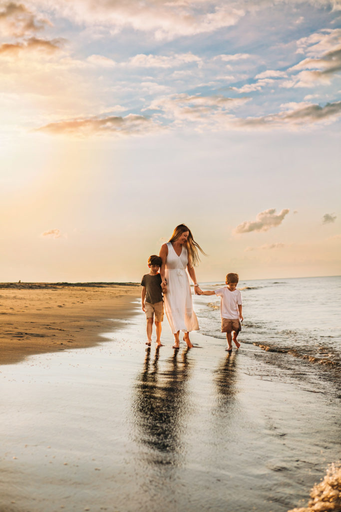 A mother walking with her sons on the beach at sunset 