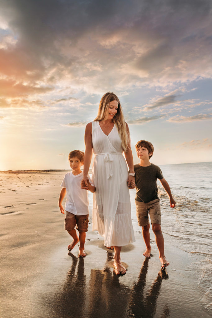 A mother walking on the beach at sunset, looking down and smiling at her sons as they hold hands