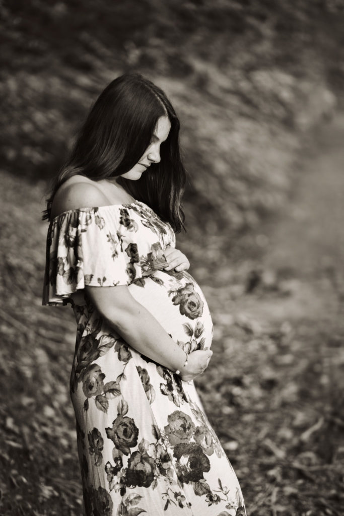 Pregnant woman holding belly during maternity photo session on Forbidden Drive in Philadelphia