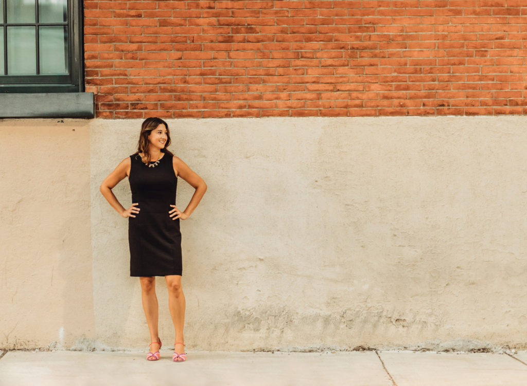 Professional woman in black dress standing in front of brick wall
