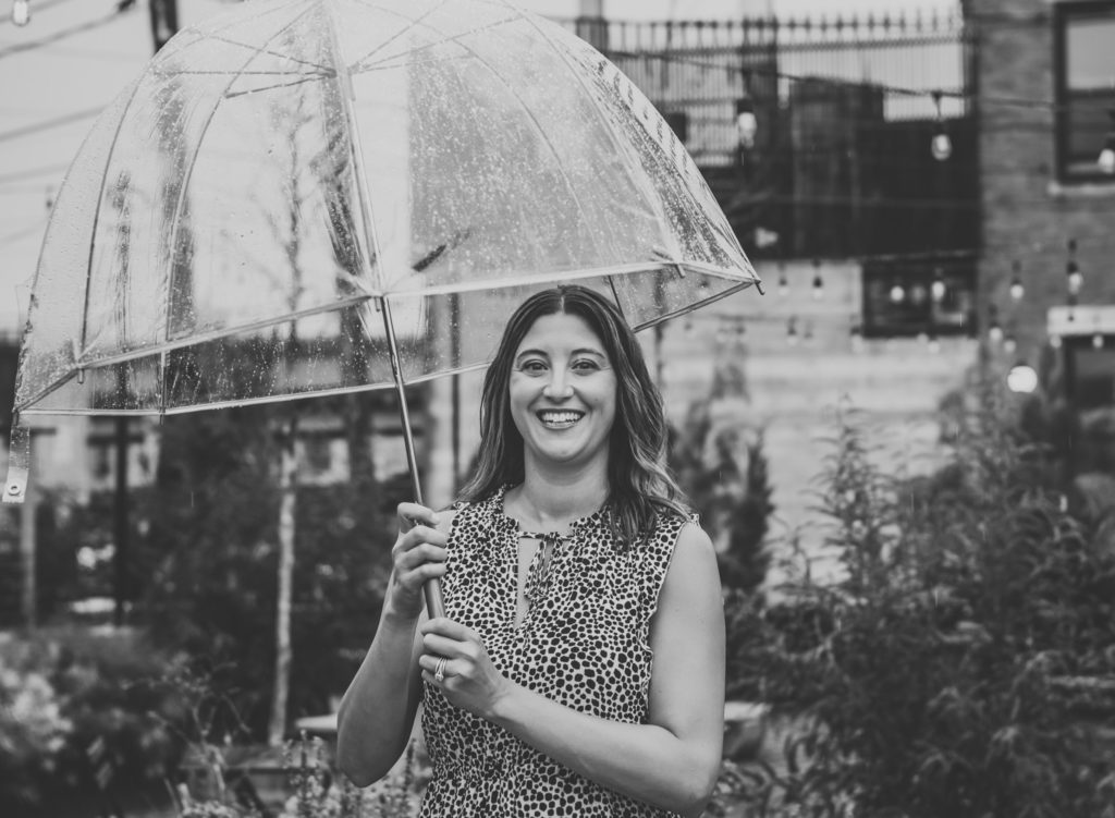 Black and white photo of woman smiling in the rain with an umbrella
