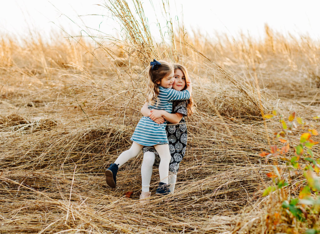 Two young daughters hugging in a field of tall grass at sunset