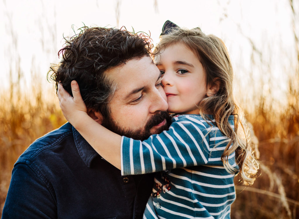 A father in a field at sunset whispering in his young daughter's ear.