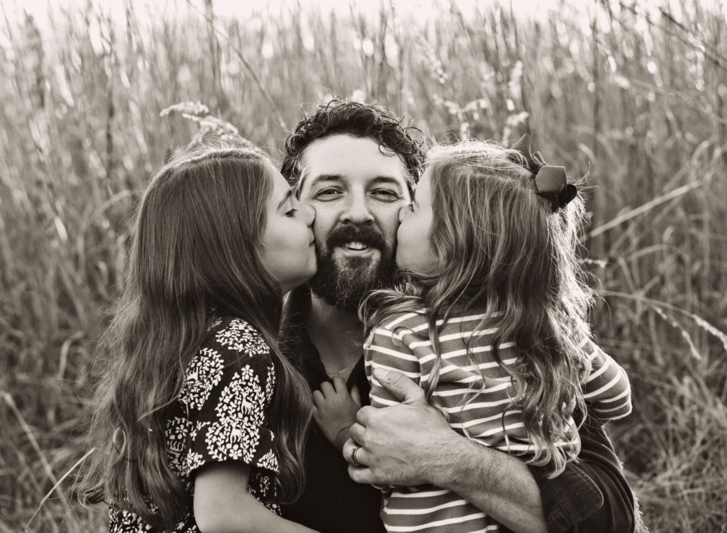 A father being kissed on each cheek by his young daughters.
