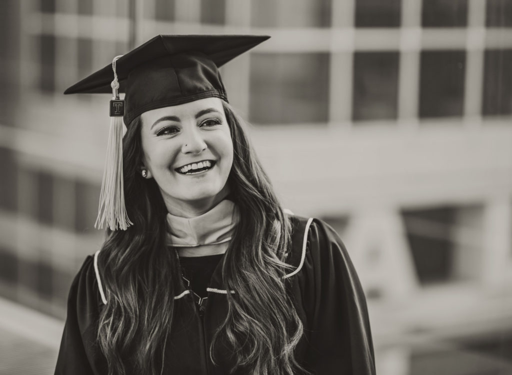 Black and white image of a woman looking off to the side and laughing while wearing a graduation hat on her head.