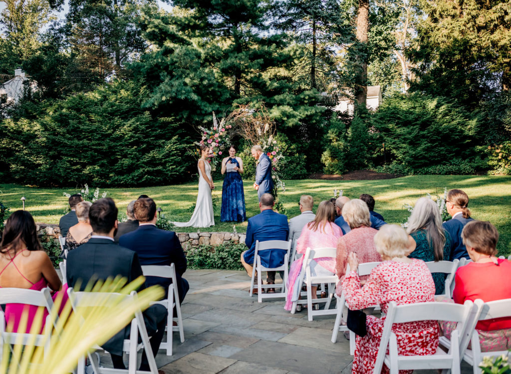 Bride and groom getting married in front of a floral arch in a backyard