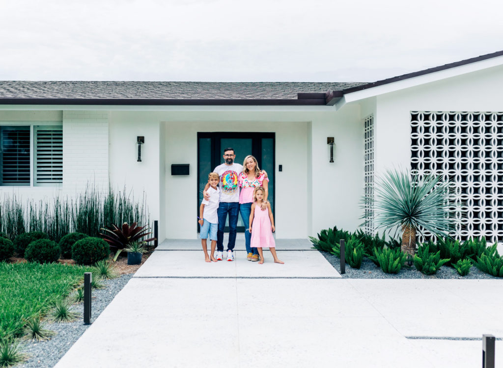 A family of four gathered in front of they white home for an in-home family photography session.