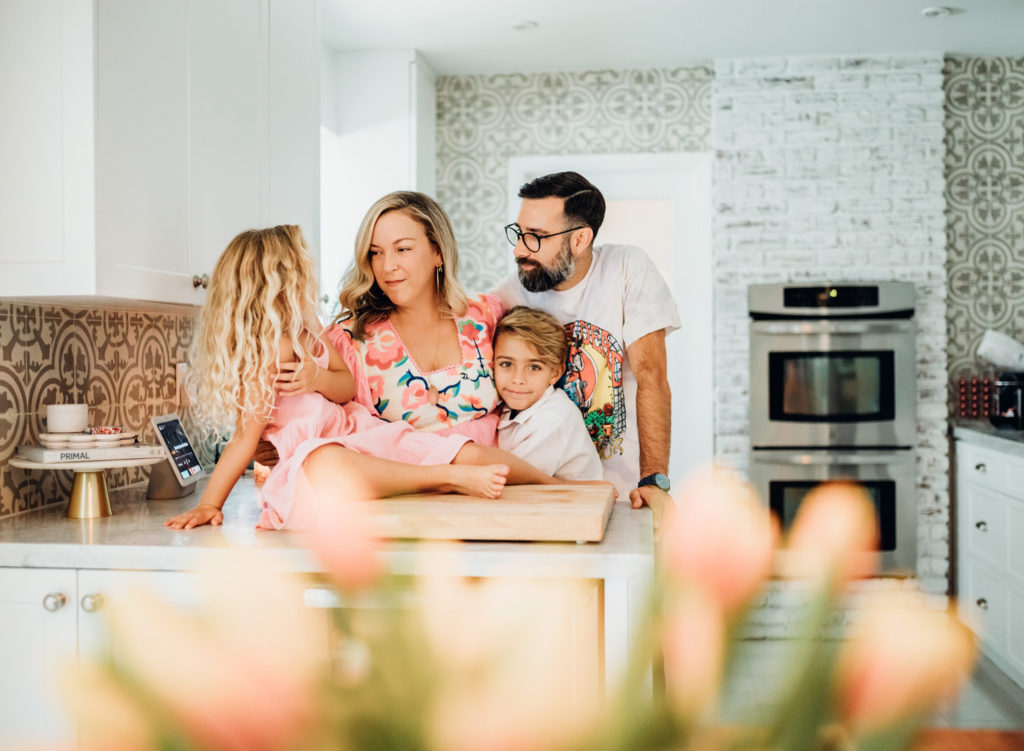 A family of four gathered together in a white kitchen for an in-home family photography session.