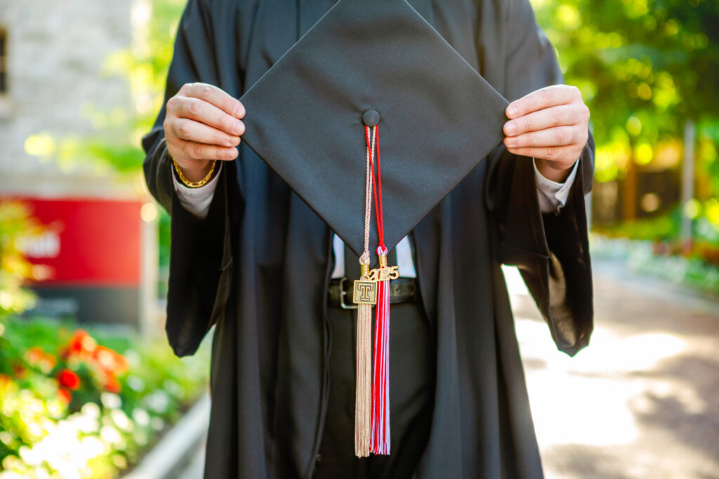 Close-up of a graduation cap held at chest level, showing tassels and a class of 2025 charm.