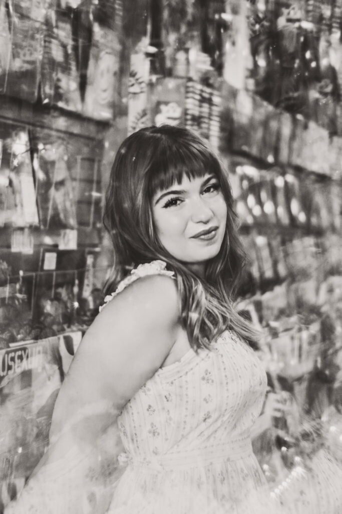 Black and white senior portrait of Lyla posing inside a record store with vinyl albums in the background with a prism effect over her.