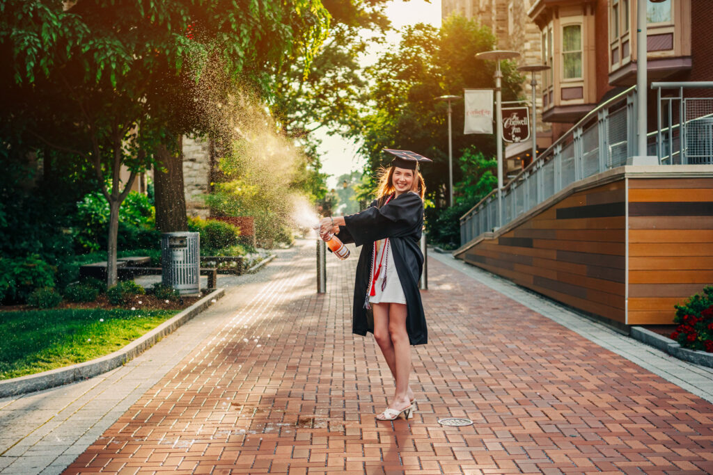Graduate popping a champagne bottle on a brick walkway during a celebratory graduation photoshoot.