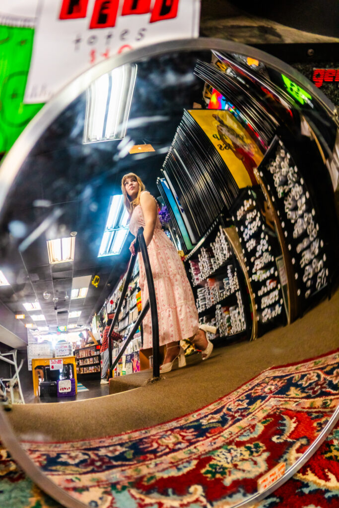 Creative senior portrait captured through a curved mirror reflection inside a record store.