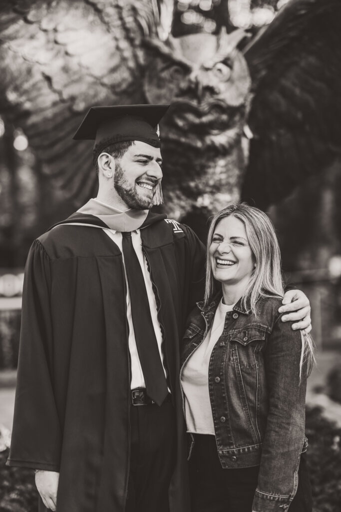 Black-and-white portrait of a graduate laughing with his mother during a graduation photoshoot.
