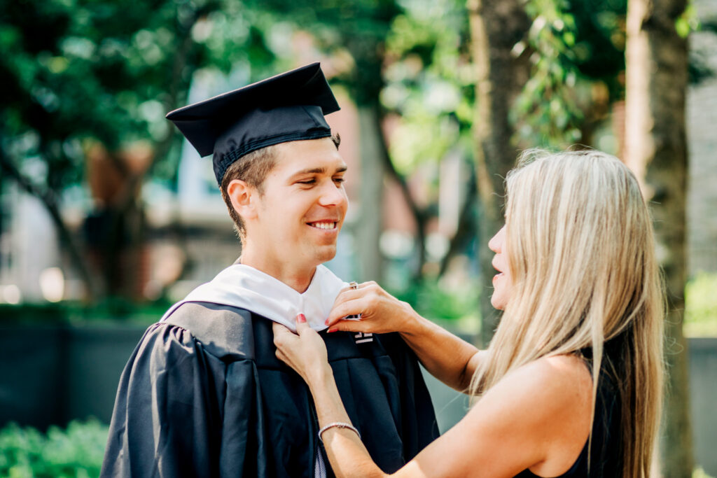 Mother adjusts her son’s graduation hood as he smiles during a Temple University graduation photoshoot.