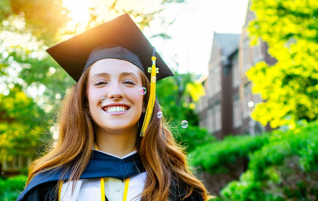Graduate smiling as bubbles float around her during an outdoor graduation portrait session.