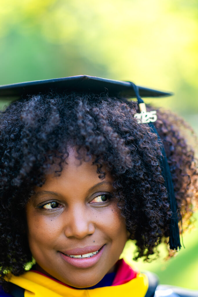 Close-up portrait of a graduate wearing a graduation cap, with soft natural light and greenery in the background
