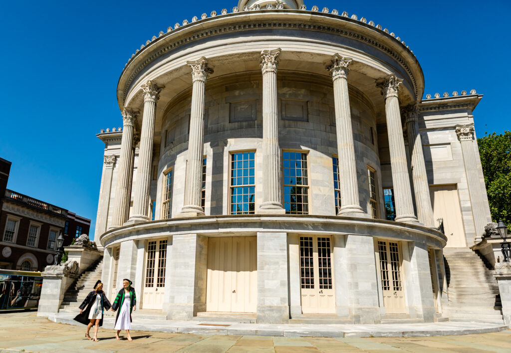 College graduates walking hand-in-hand outside a historic building during a graduation photoshoot in Philadelphia
