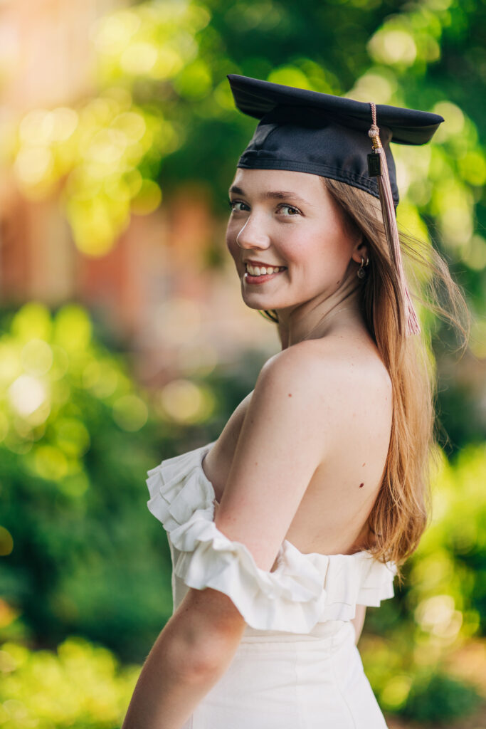 College graduate styled for a graduation photoshoot in Philadelphia, wearing a cap and gown and white dress outdoors