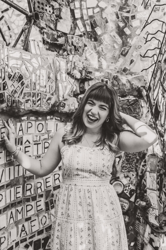 Black and white senior portrait of Lyla laughing with her hands lifted against a textured mosaic wall