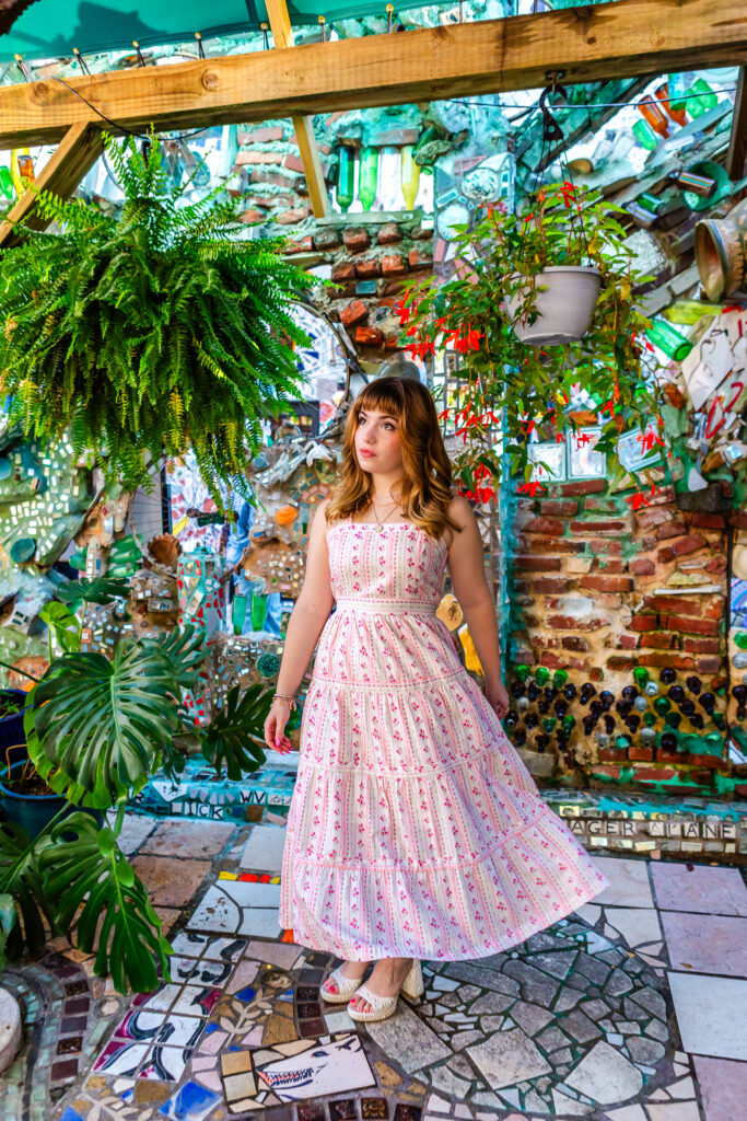 Full-body senior portrait of Lyla twirling her pink and white dress surrounded by mosaic art and greenery.