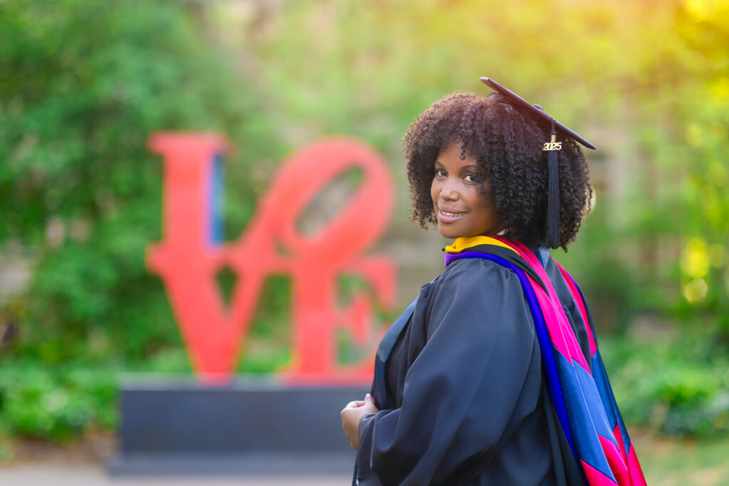 Graduate wearing a cap and gown during a graduation photoshoot, looking over her shoulder with the Love Statue behind her.