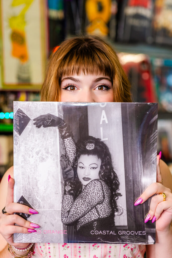 Creative senior portrait of Lyla holding a vinyl record called "Coastal Grooves" partially in front of her face.