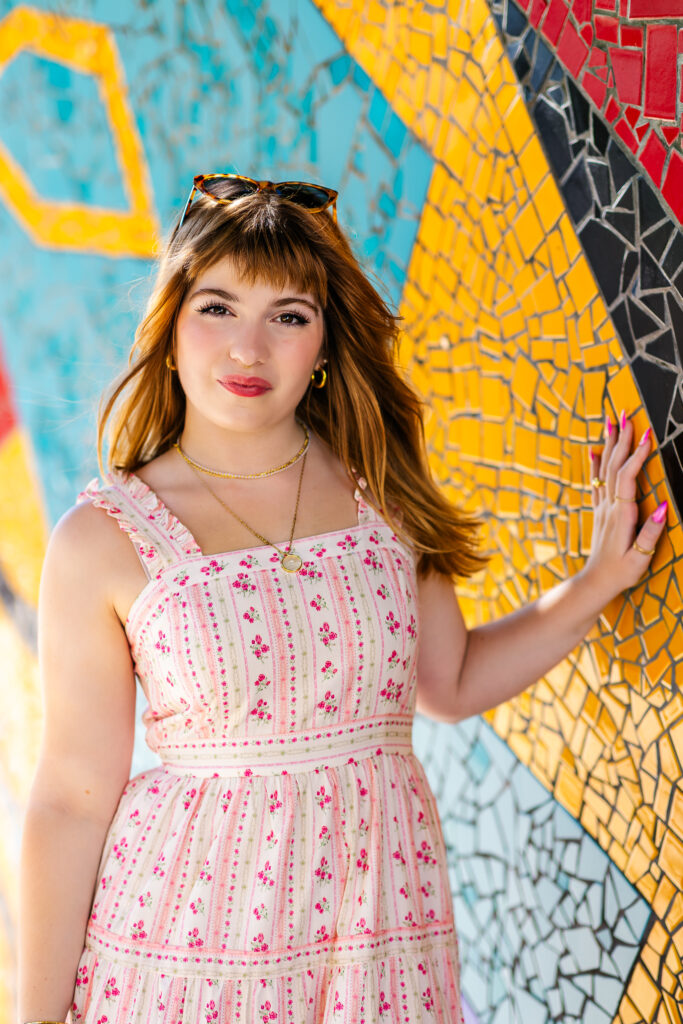 Senior portrait of Lyla standing against a colorful mosaic wall on South Street in Philadelphia.